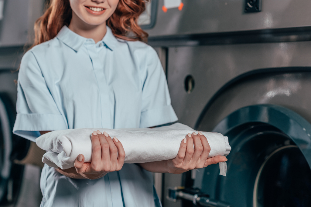 female dry cleaning worker holding stack of clean white clothes