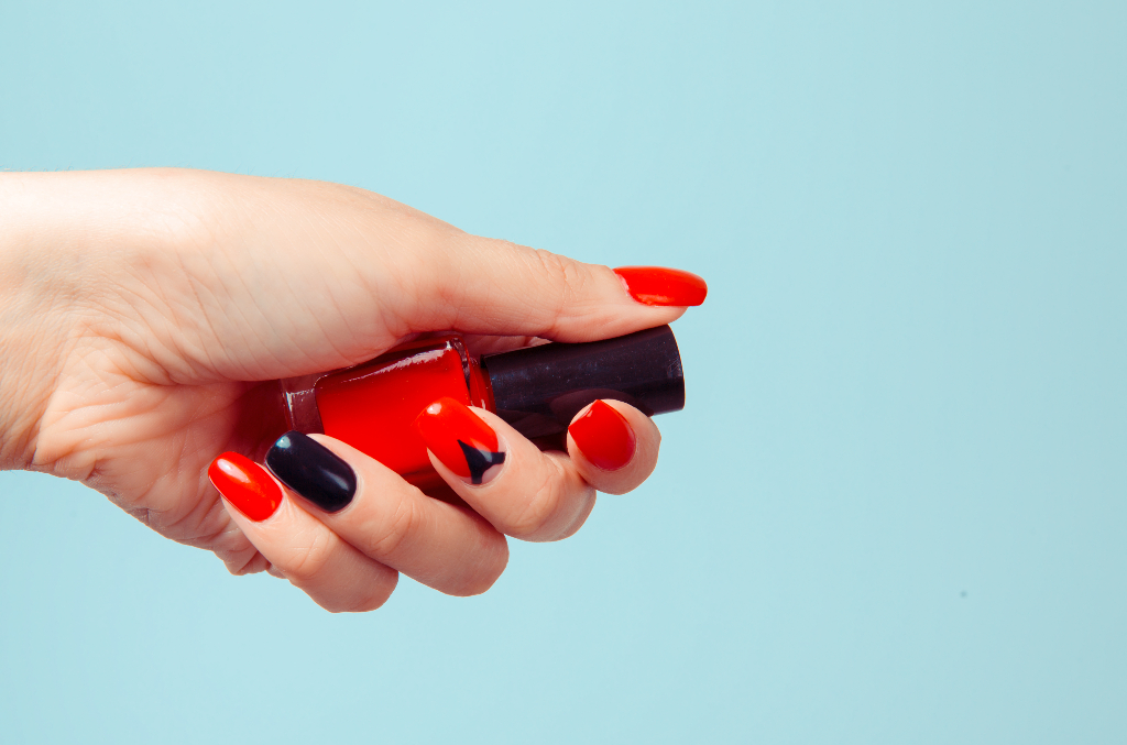 female with a red and black manicure while holding a bottle of red nail polish