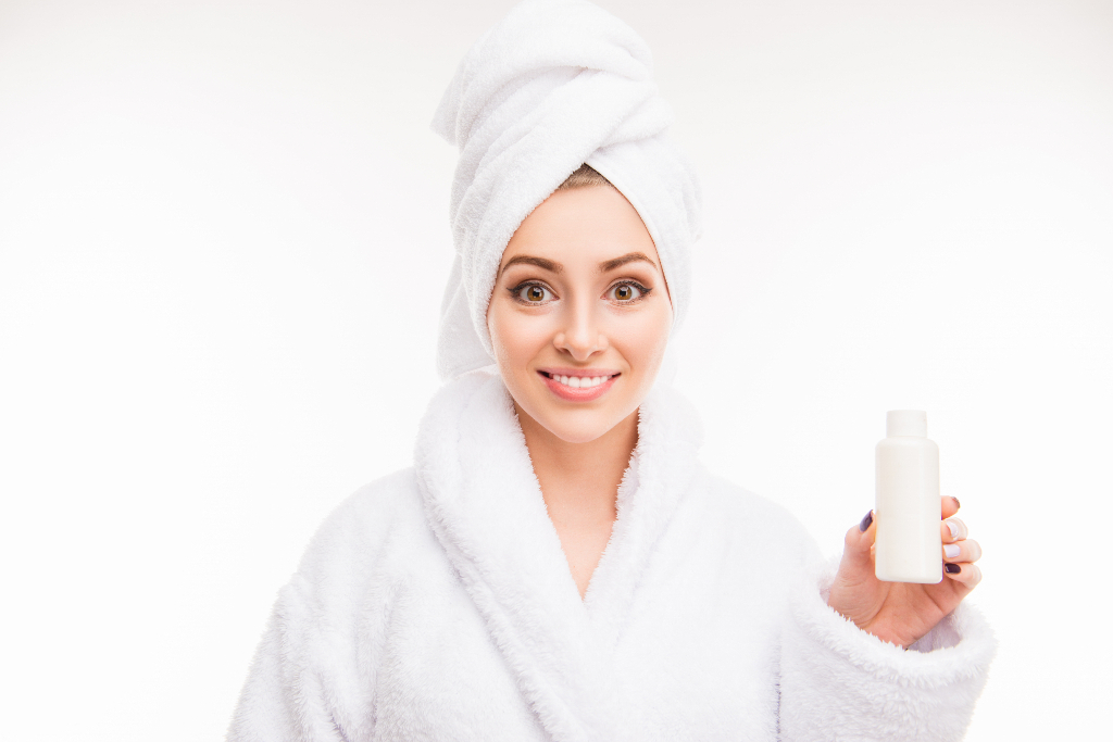 girl with towel on her head while holding a bottle of shampoo