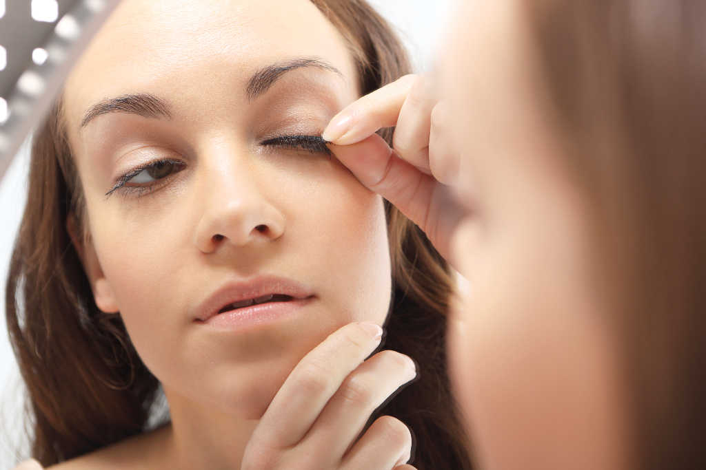 woman attaching fake eyelashes on her eyes