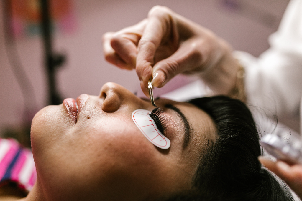 woman holding a tweezer while applying fake eyelashes to her client